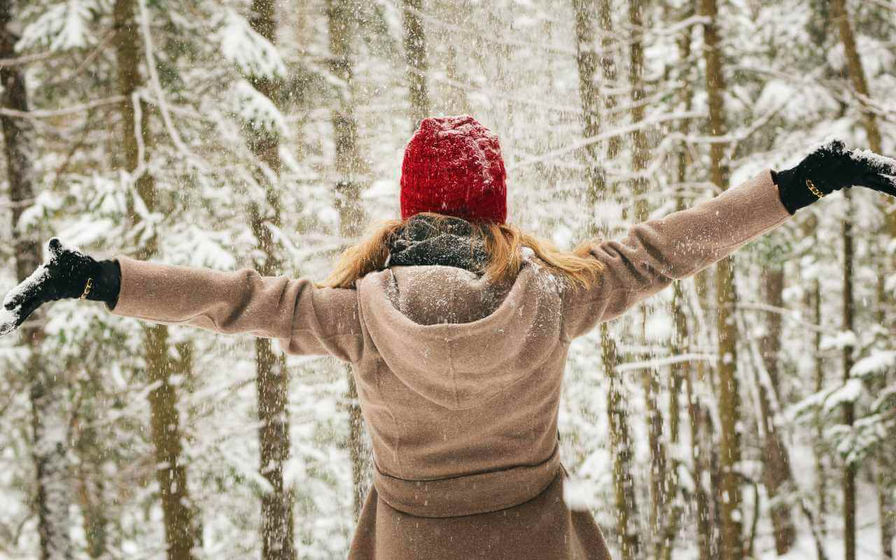 Devojka na snegu sa crvenom kapom. srećno raširila ruke - kadar sa leđa.