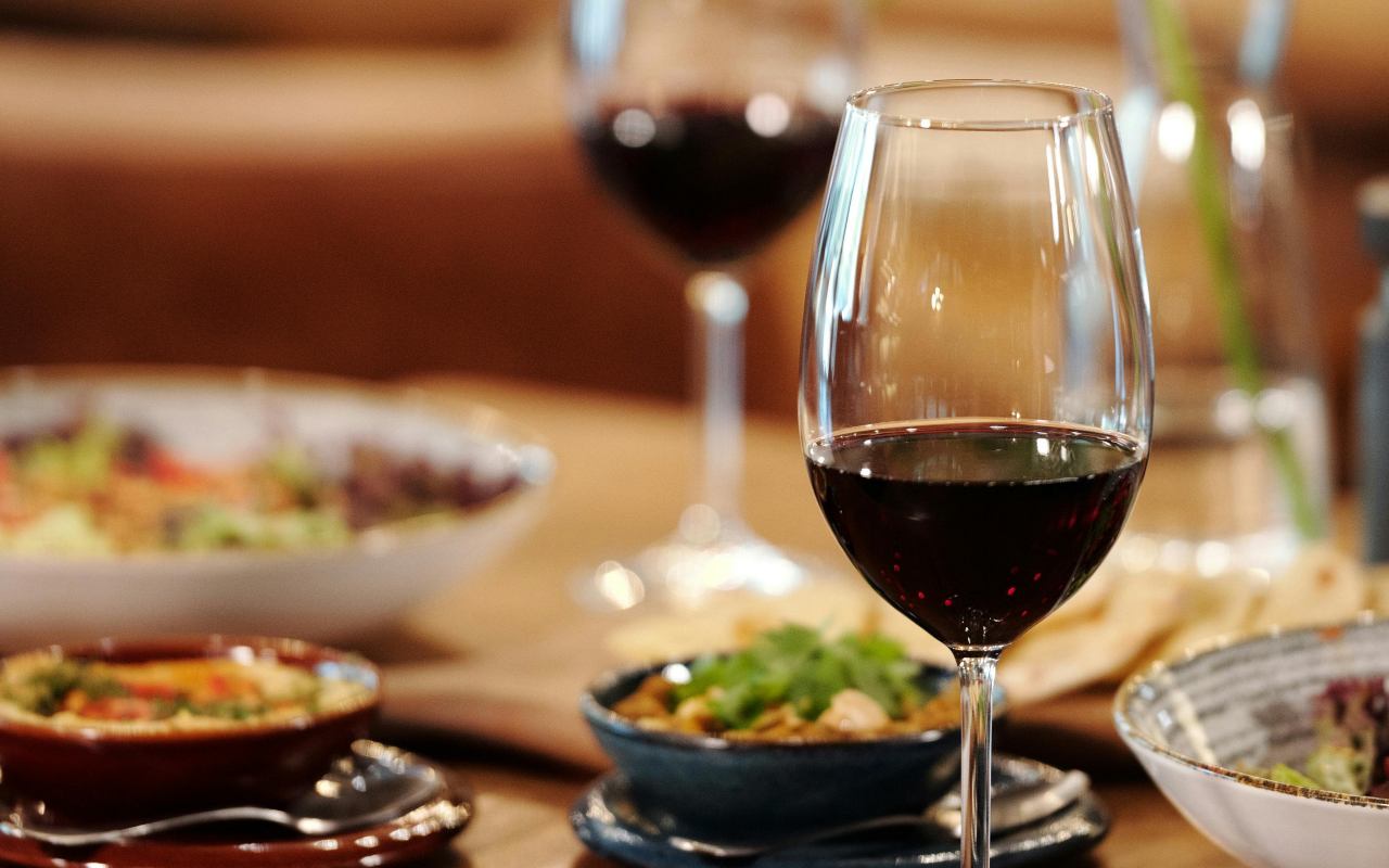  Dve čaše crnog vina na stolu pored tanjira sa hranom